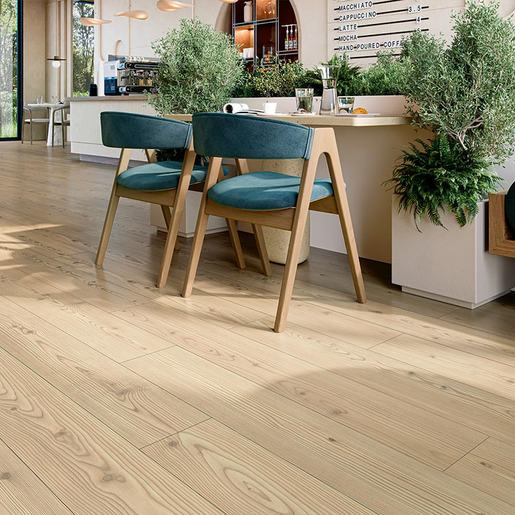lichte houten vloer met brede planken en natuurlijke houtnerfstructuur in licht beige kleur, geplaatst in moderne ruimte met groene planten en blauwe stoelen