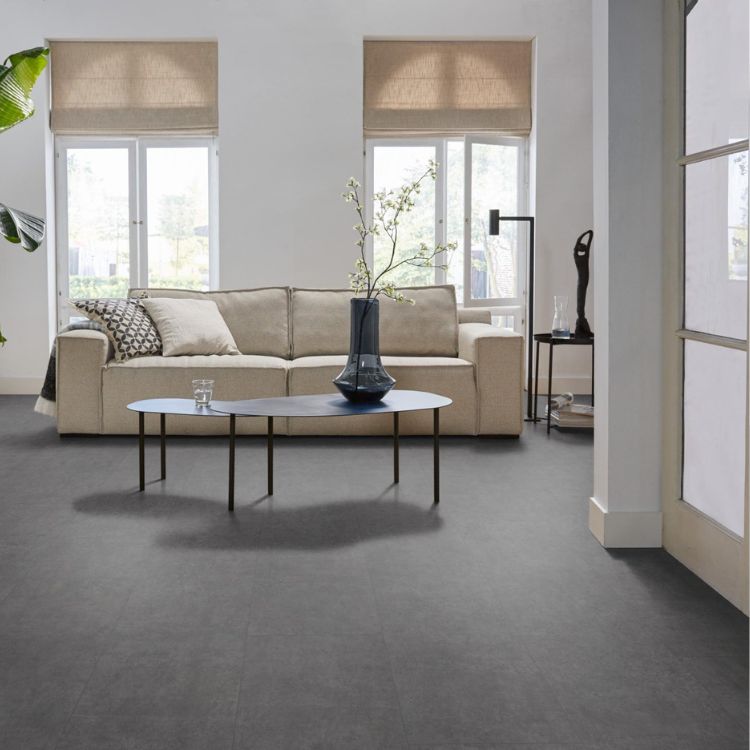 donkergrijze tegelvloer met grote matte tegels en subtiel golvend streeppatroon in een lichte woonkamer met beige bank en ronde zwarte salontafel