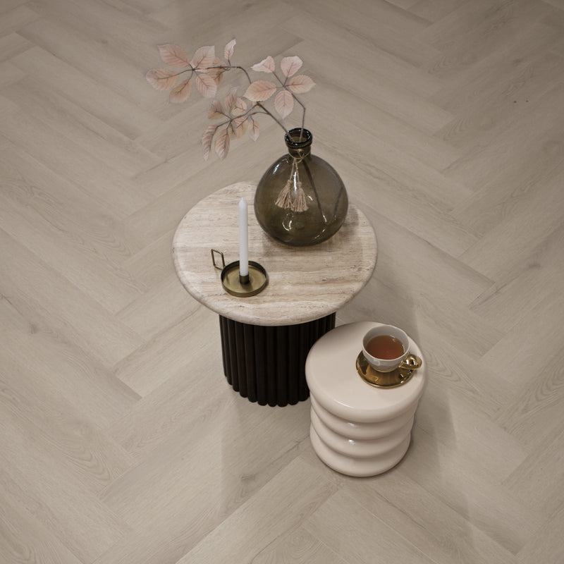licht eiken visgraatvloer met natuurlijke houtstructuur en brede planken, lichte beige ondertoon, gecombineerd met ronde stenen bijzettafel met glazen vaas en witte kaars
