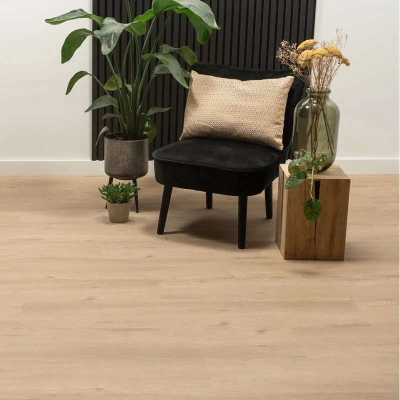 Licht beige eiken vloer met brede planken en een subtiele houtstructuur, gecombineerd met een zwart fluwelen stoel, een sierkussen in beige met een fijn geometrisch patroon, een grote groenbladige plant in een grijze pot en een houten bijzettafel met een glazen vaas gevuld met droge bloemen.