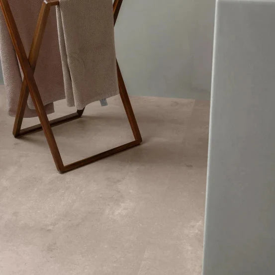 lichte beige tegelvloer met subtiele, vloeiende streken en matte structuur, gecombineerd met een bruine houten kledingstandaard met zachte beige stoffen doeken