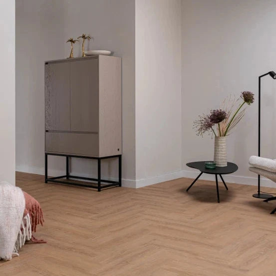 licht beige eiken vloer met visgraat patroon en brede planken in moderne, minimalistische woonkamer met grijs kastje en zwart metalen bijzettafeltje met vaas en bloemen