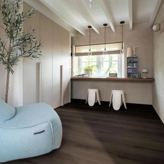 donkerbruine vloer met brede planken in rechte lengte, modern interieur met beige kastenwand en lichtblauwe stoffen fauteuil naast een houten werkblad en witte barkrukken onder plafondbalken