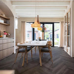 donkergrijs visgraatvloer met brede planken in modern interieur, strak houten eettafel met beige stoffen stoelen, open ruimte met grote ramen en lichte muren
