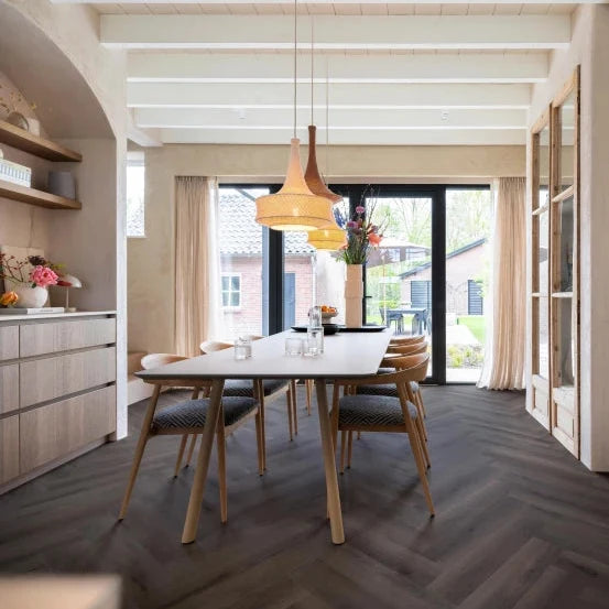 donkergrijs visgraatvloer met brede planken in modern interieur, strak houten eettafel met beige stoffen stoelen, open ruimte met grote ramen en lichte muren