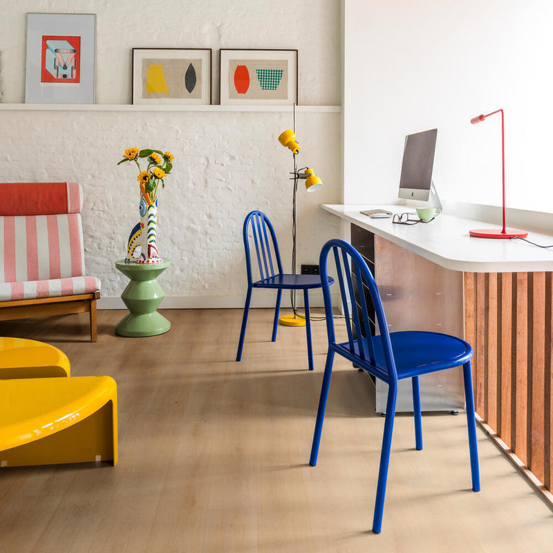 lichte eiken vloer met brede planken en subtiele houtstructuur in een modern interieur met blauwe metalen stoelen, gele vloerlamp, wit bureau met rood bureaulampje en kleurrijke wanddecoratie