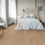 lichte vloer in beige eiken kleur met fijne houtnerfstructuur en brede planken in een lichte slaapkameromgeving met wit linnen beddengoed en een bloemenpatroon hoofdeinde