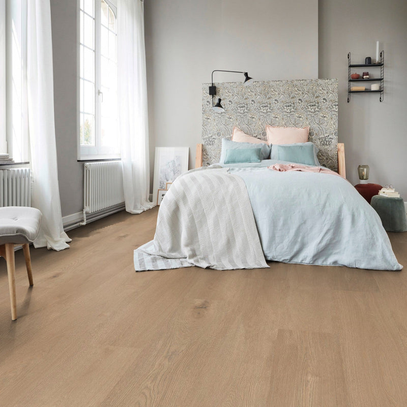 lichte vloer in beige eiken kleur met fijne houtnerfstructuur en brede planken in een lichte slaapkameromgeving met wit linnen beddengoed en een bloemenpatroon hoofdeinde